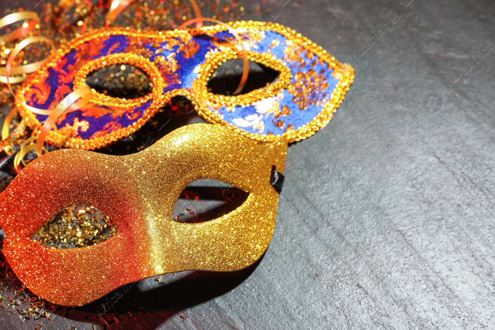 Photo of Beautiful carnival masks on gray textured table, closeup. Space for text