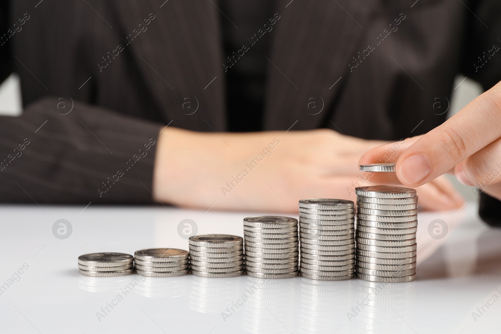 Photo of Salary concept. Woman putting coin on stack at white table, closeup