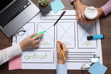 Photo of Developing UI design. Designers creating website wireframe on paper at wooden table, top view