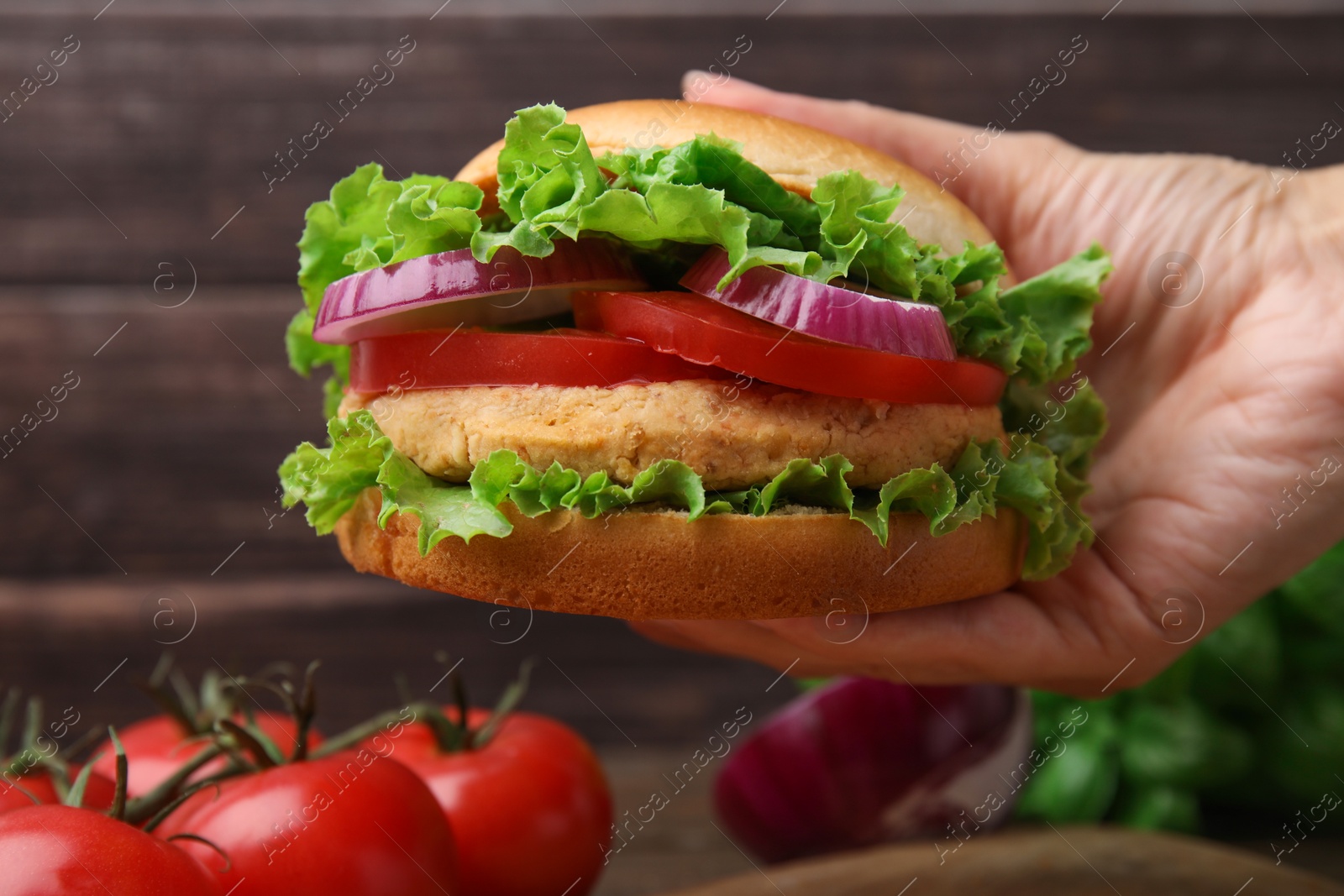 Photo of Woman holding vegetarian burger with chickpea cutlet at table, closeup