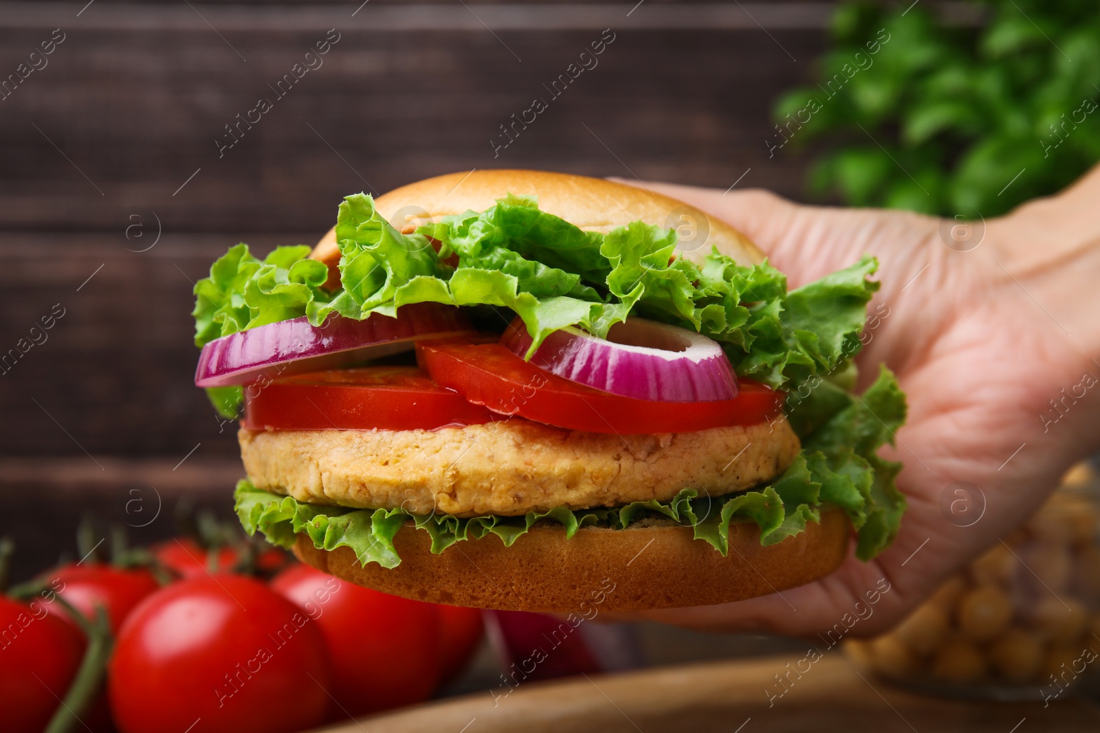 Photo of Woman holding vegetarian burger with chickpea cutlet at table, closeup