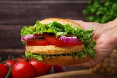 Photo of Woman holding vegetarian burger with chickpea cutlet at table, closeup