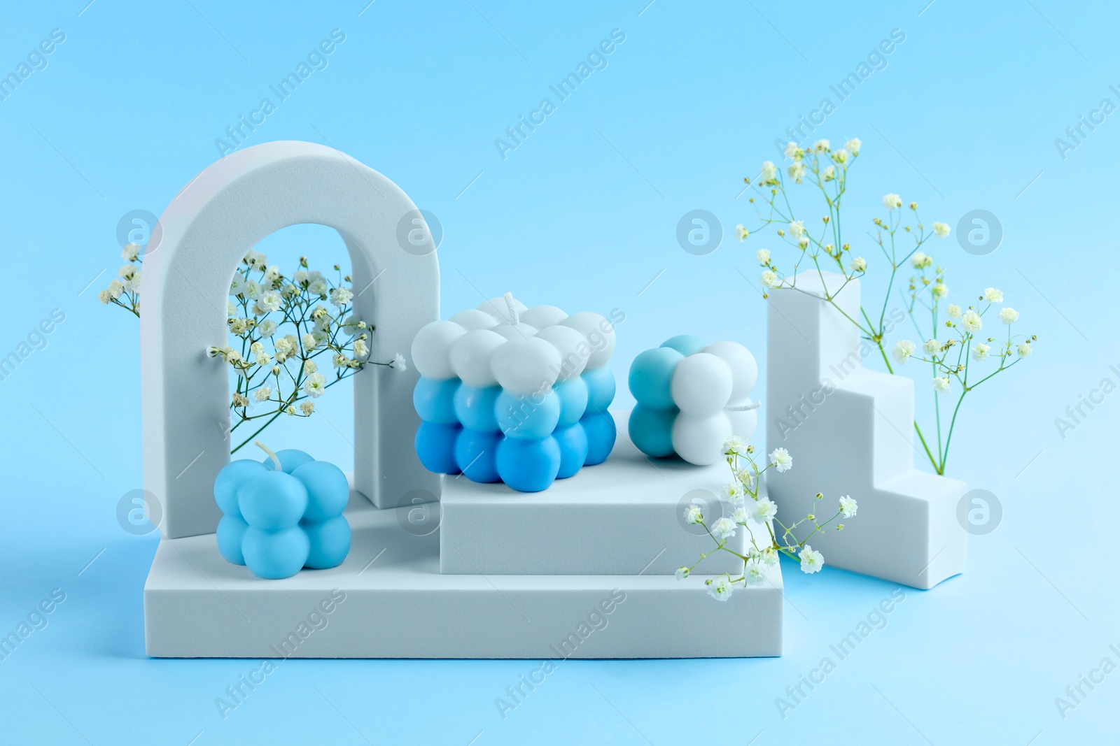 Photo of Beautiful bubble candles, gypsophila flowers and geometric figures on light blue background