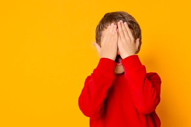 Photo of Scared little boy covering face on orange background. Space for text