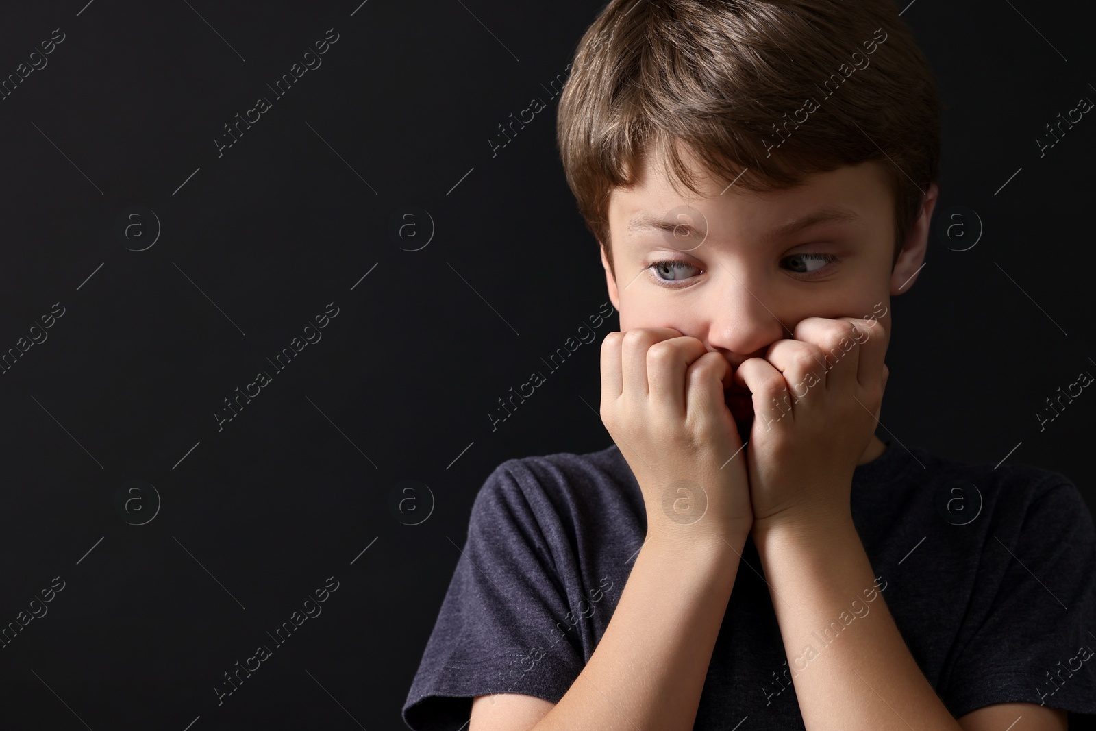 Photo of Scared little boy on black background. Space for text