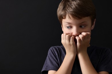 Photo of Scared little boy on black background. Space for text