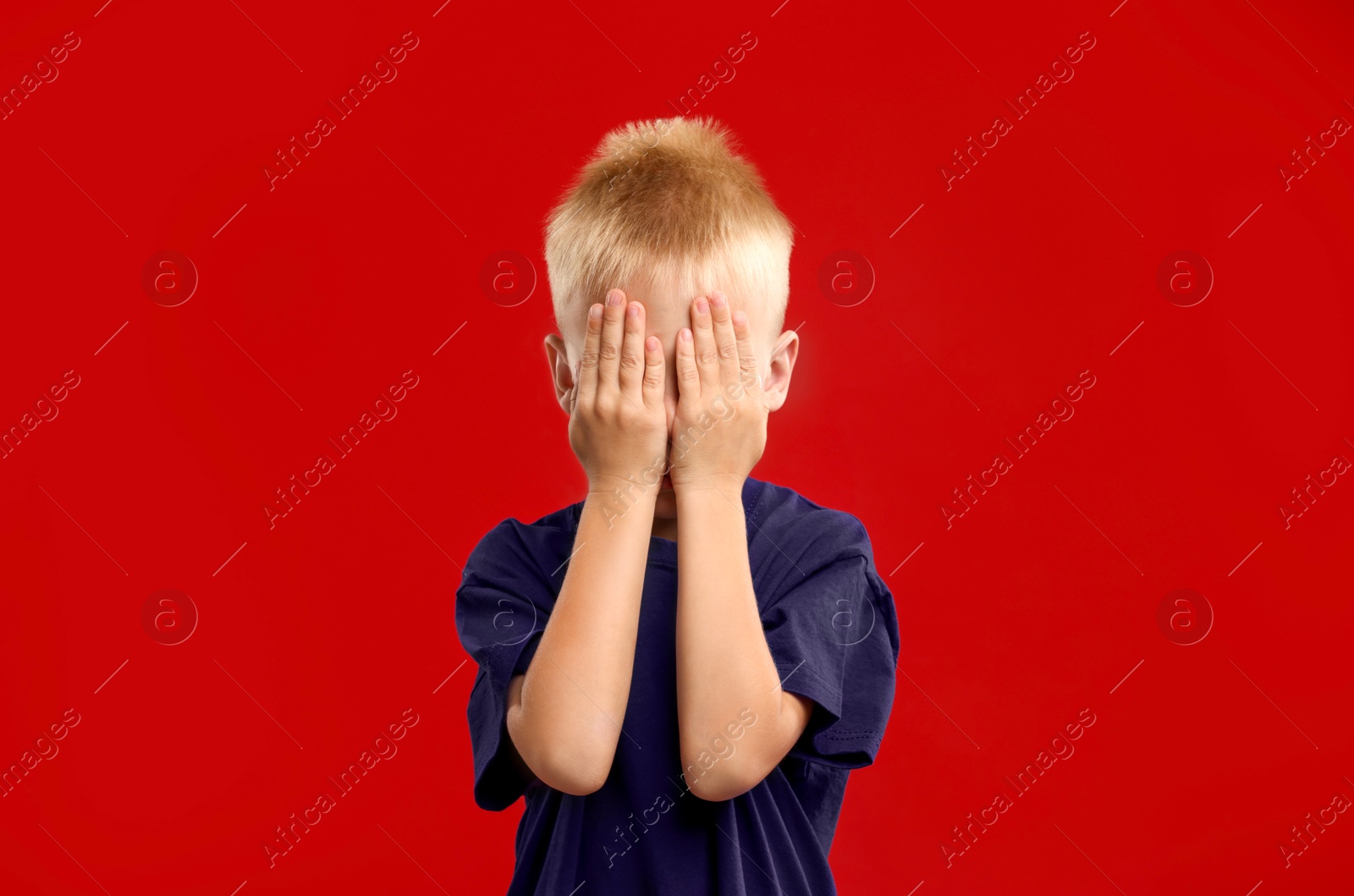 Photo of Scared little boy covering face with hands on red background