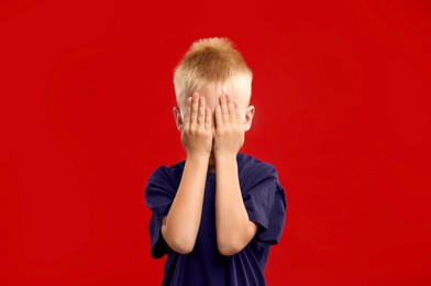 Photo of Scared little boy covering face with hands on red background