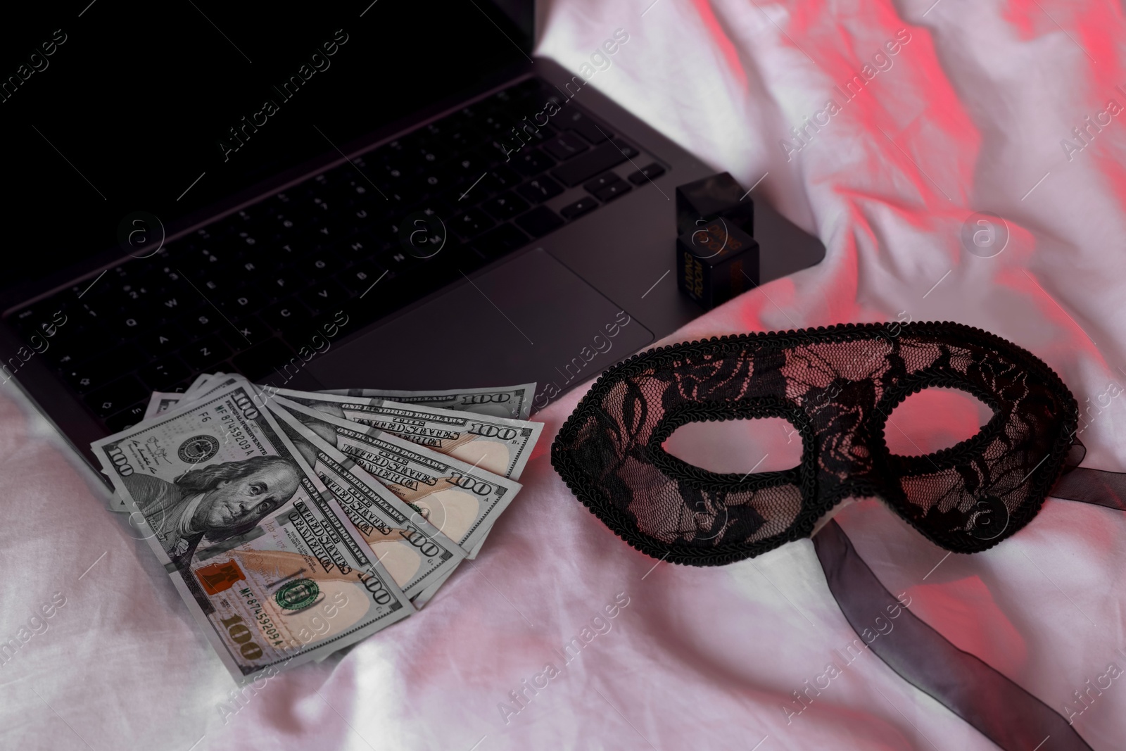 Photo of Prostitution and virtual sex. Laptop, dollar banknotes and mask on linens