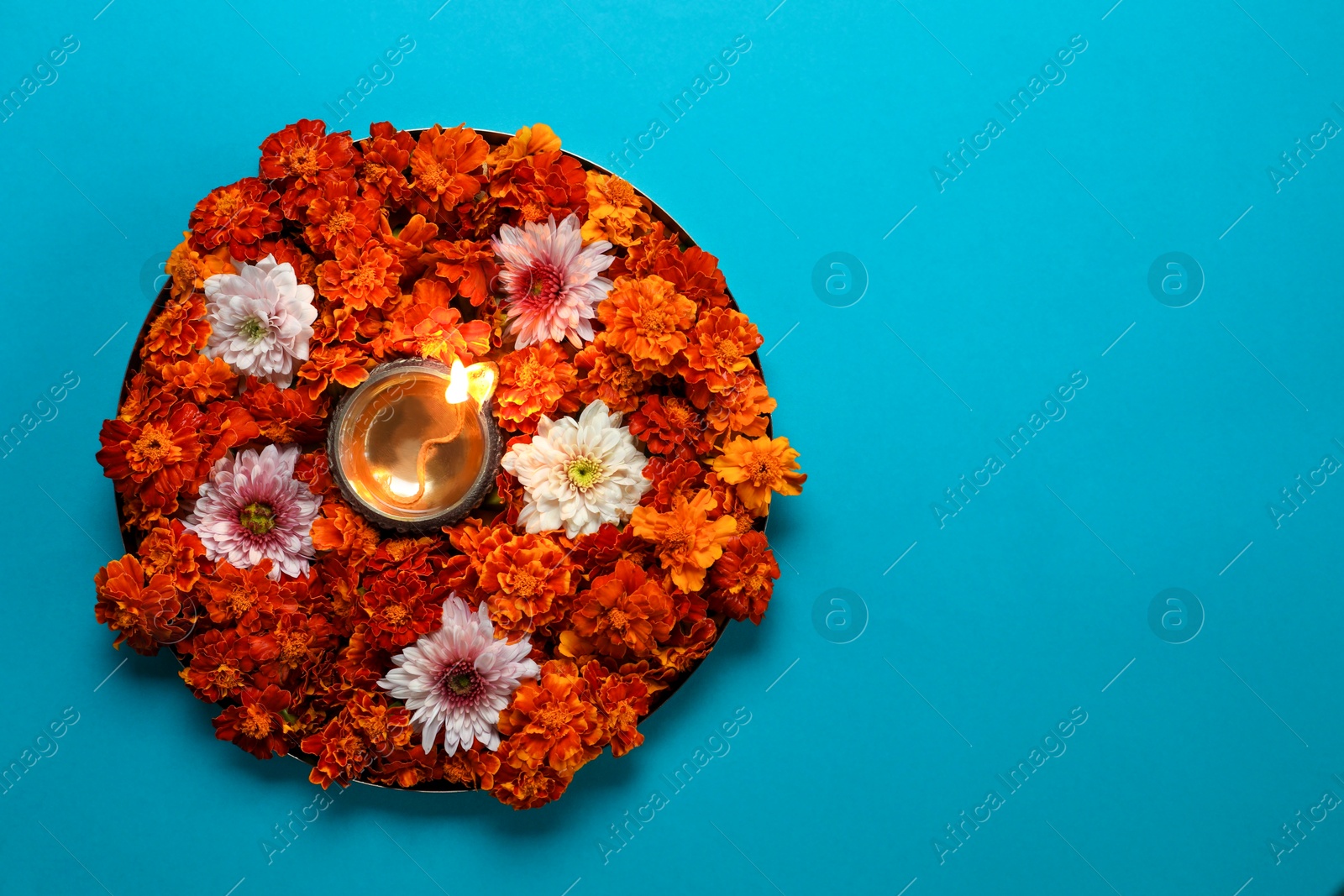 Photo of Diwali celebration. Diya lamp and beautiful flowers on turquoise background, top view. Space for text