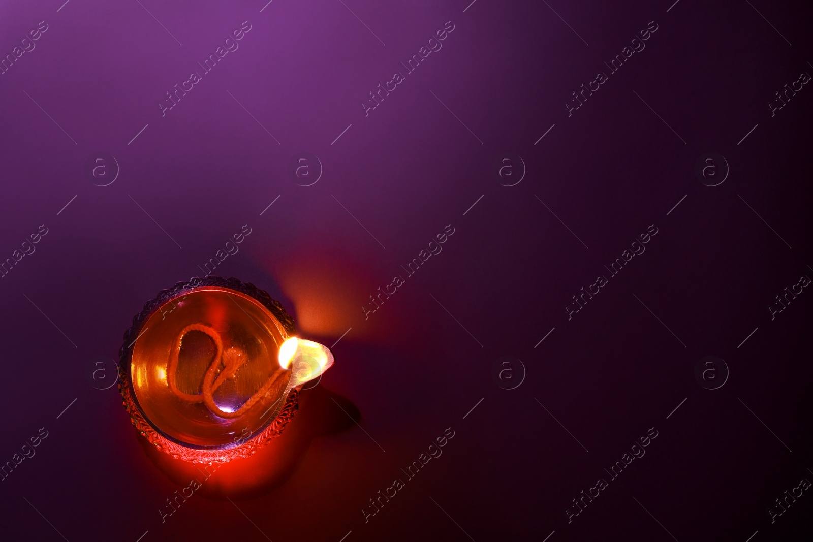 Photo of Diwali celebration. Diya lamp on purple background, top view. Space for text