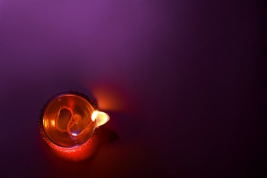 Photo of Diwali celebration. Diya lamp on purple background, top view. Space for text