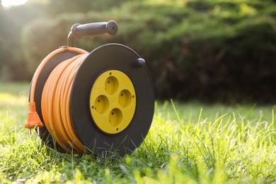 Photo of One extension cord reel on green grass outdoors, space for text