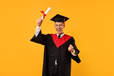 Photo of Happy student with diploma after graduation on orange background