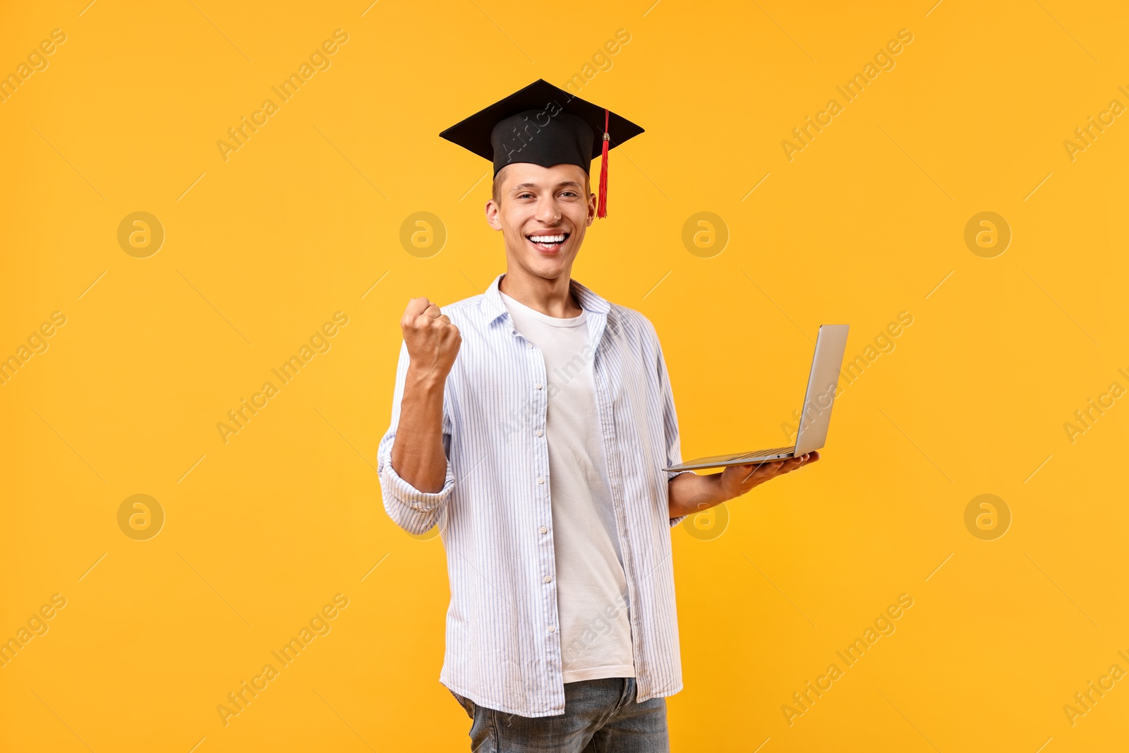 Photo of Happy student with laptop after graduation on orange background