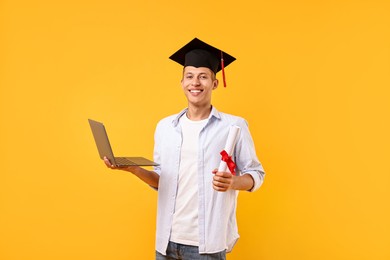 Photo of Happy student with diploma and laptop after graduation on orange background