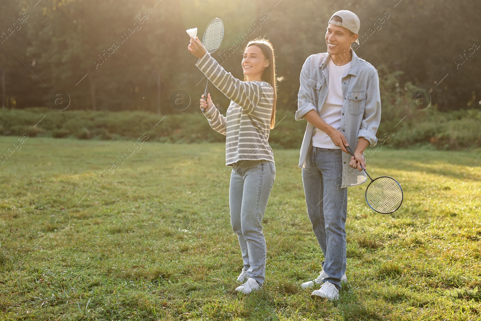 Photo of Young woman and man playing badminton in park on sunny day