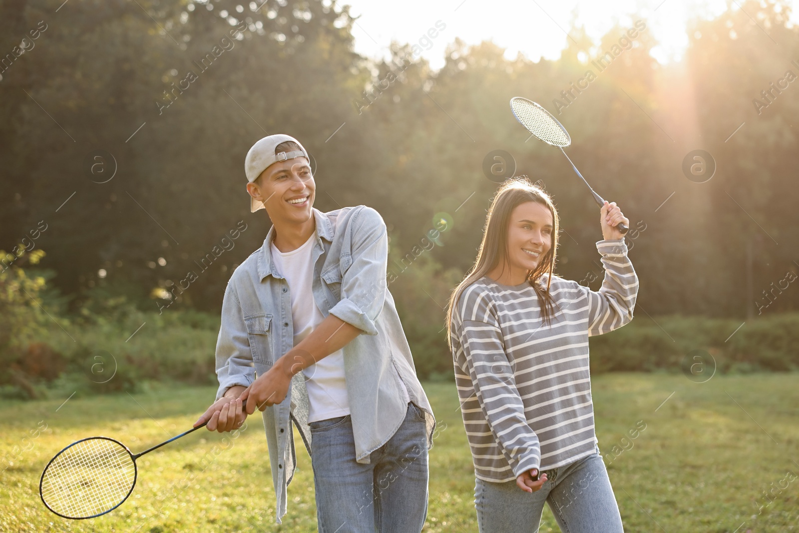 Photo of Young woman and man playing badminton in park on sunny day