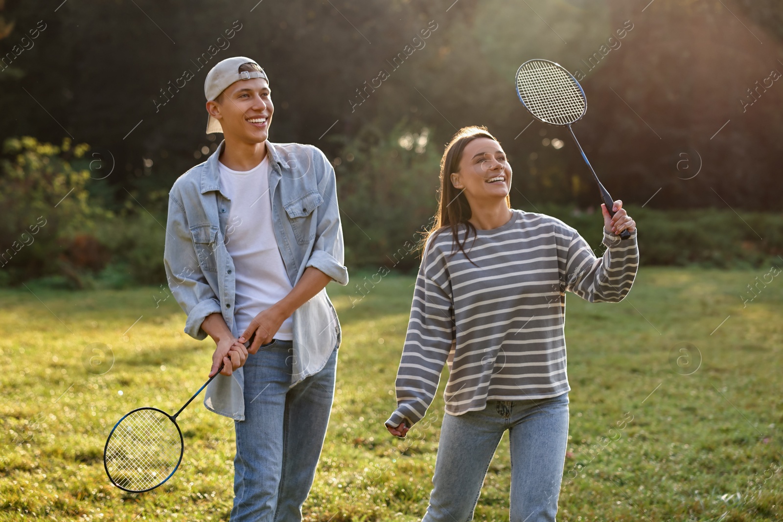 Photo of Young woman and man playing badminton in park on sunny day