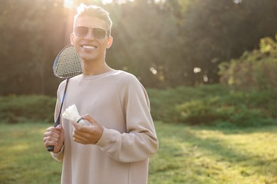 Photo of Happy young man with badminton racket and shuttlecock in park on sunny day, space for text