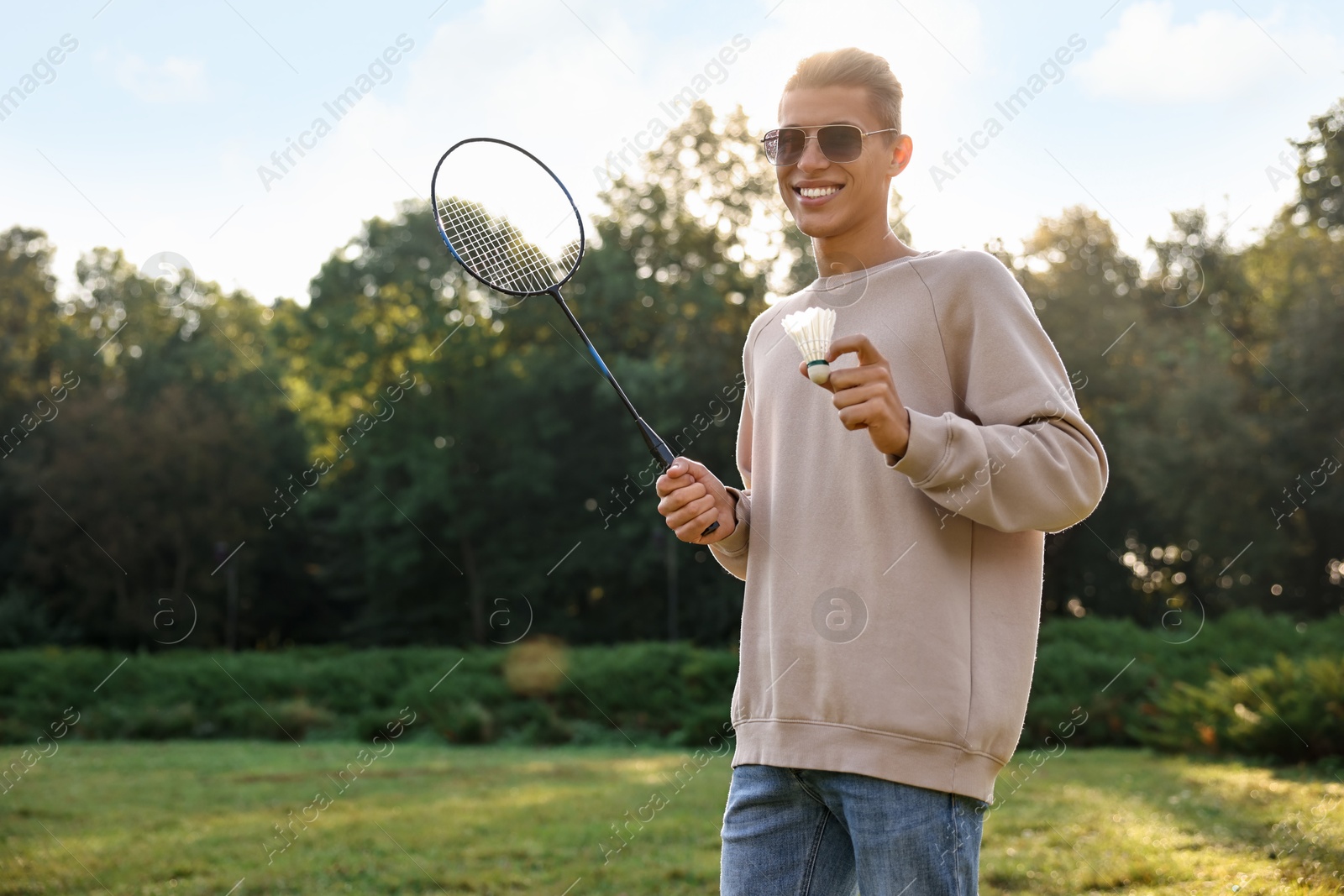 Photo of Happy young man with badminton racket and shuttlecock in park on sunny day