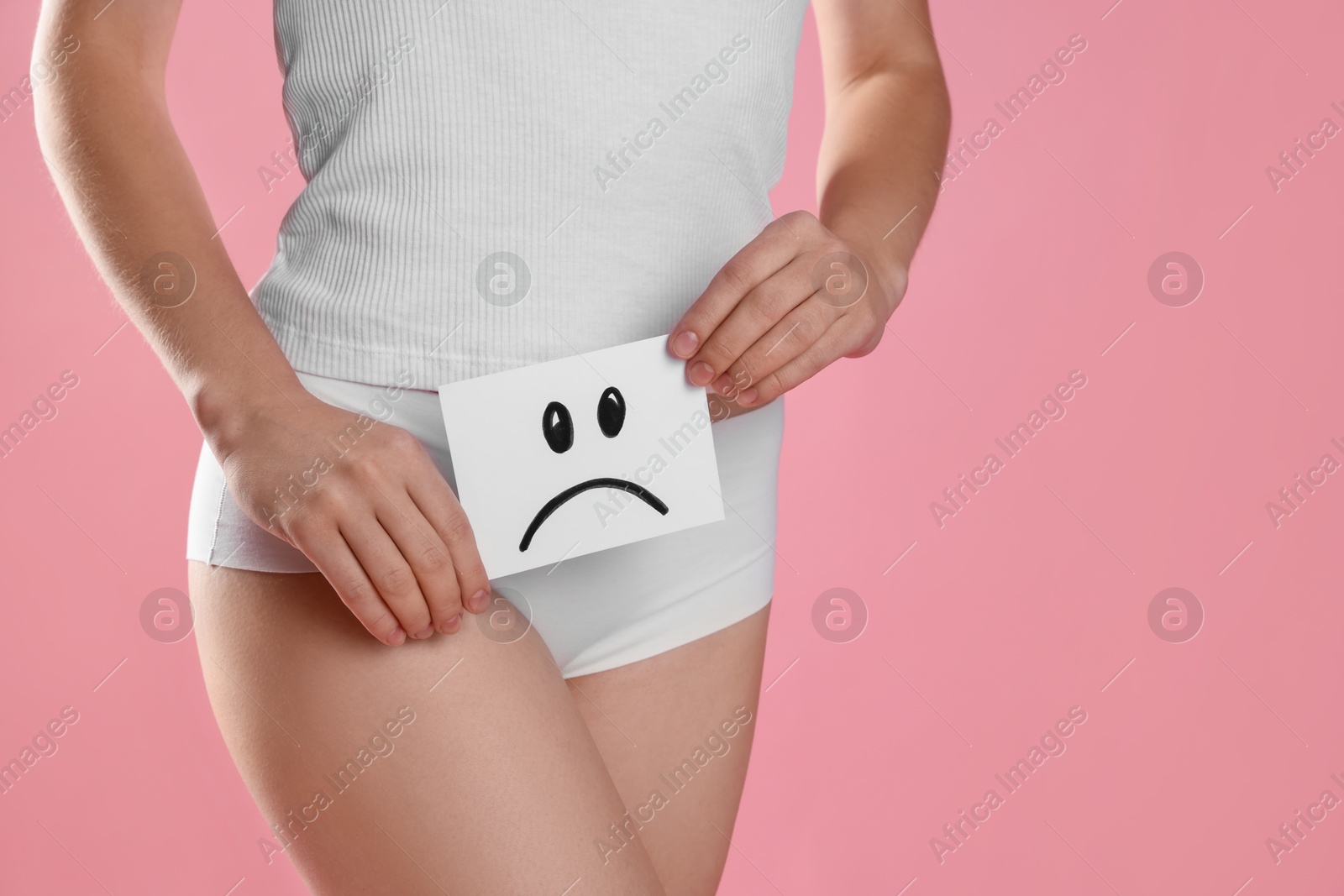 Photo of STD (sexually transmitted disease). Woman holding sticky note with drawn sad face on pink background, closeup. Space for text