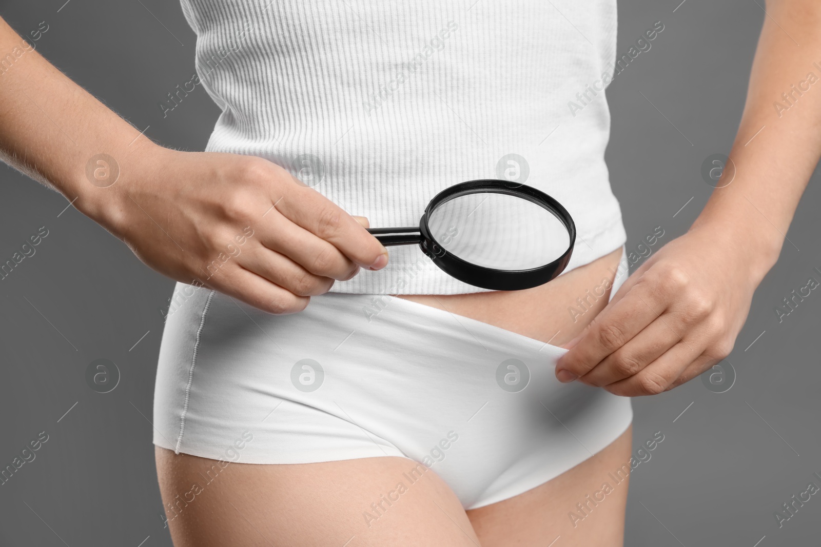 Photo of STD (sexually transmitted disease). Woman examining genital area with magnifying glass on grey background, closeup