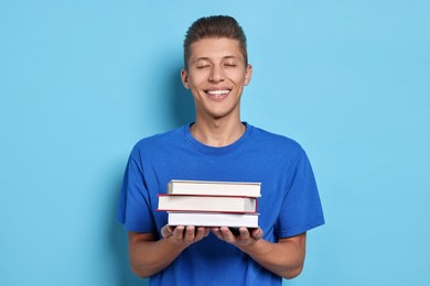 Photo of Happy student with stack of books on light blue background