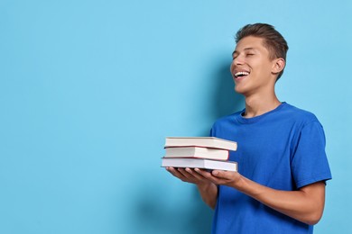 Photo of Happy student with stack of books on light blue background. Space for text