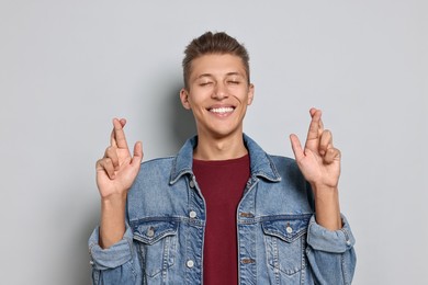 Photo of Emotional student with crossed fingers on grey background. Hope for good exam result