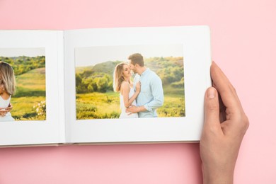 Photo of Woman looking at photos in photo album on pink background, top view