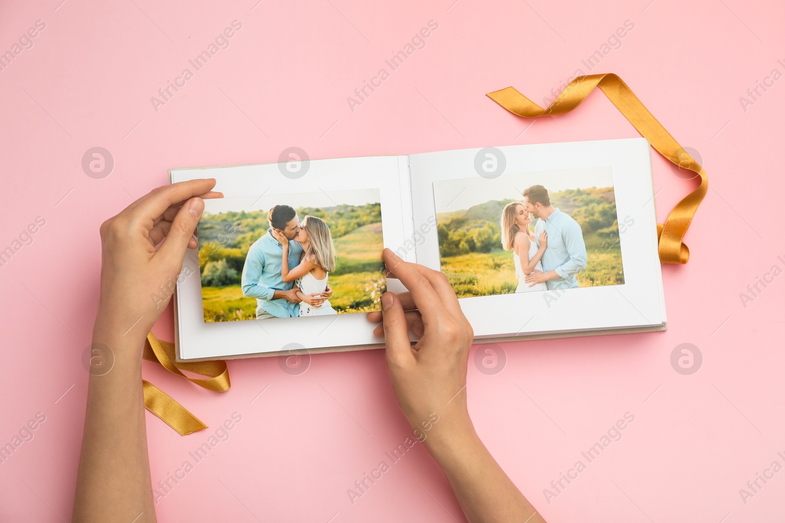 Photo of Woman looking at photos in photo album on pink background, top view