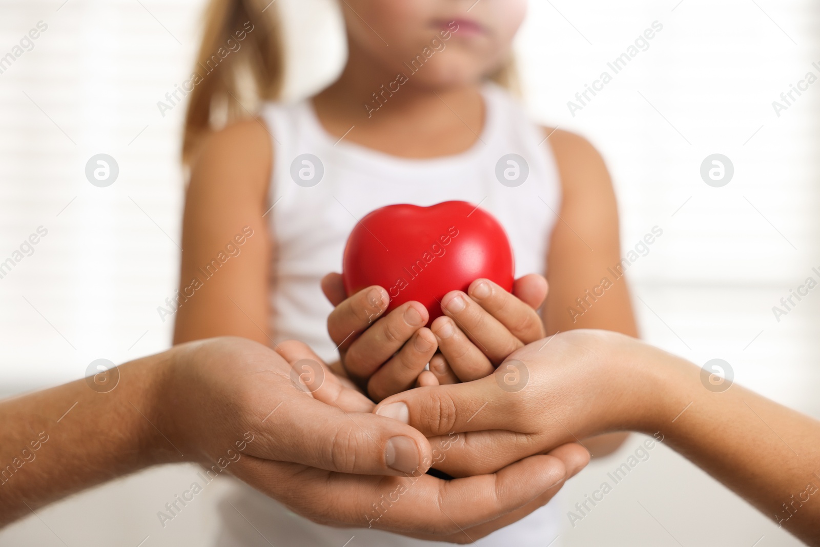 Photo of Little girl with red heart figure and her parents indoors, closeup