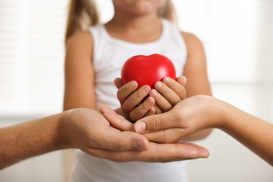 Photo of Little girl with red heart figure and her parents indoors, closeup