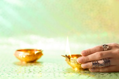 Photo of Diwali celebration. Woman with lit diya lamp on color background, closeup