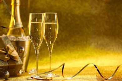 Photo of Champagne, gift box and streamers on golden background. Space for text