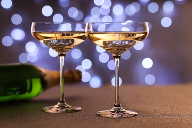 Photo of Champagne in glasses and bottle on table against blurred lights, closeup