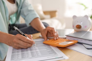 Photo of Budget planning. Woman using calculator while working with accounting document at table indoors, closeup