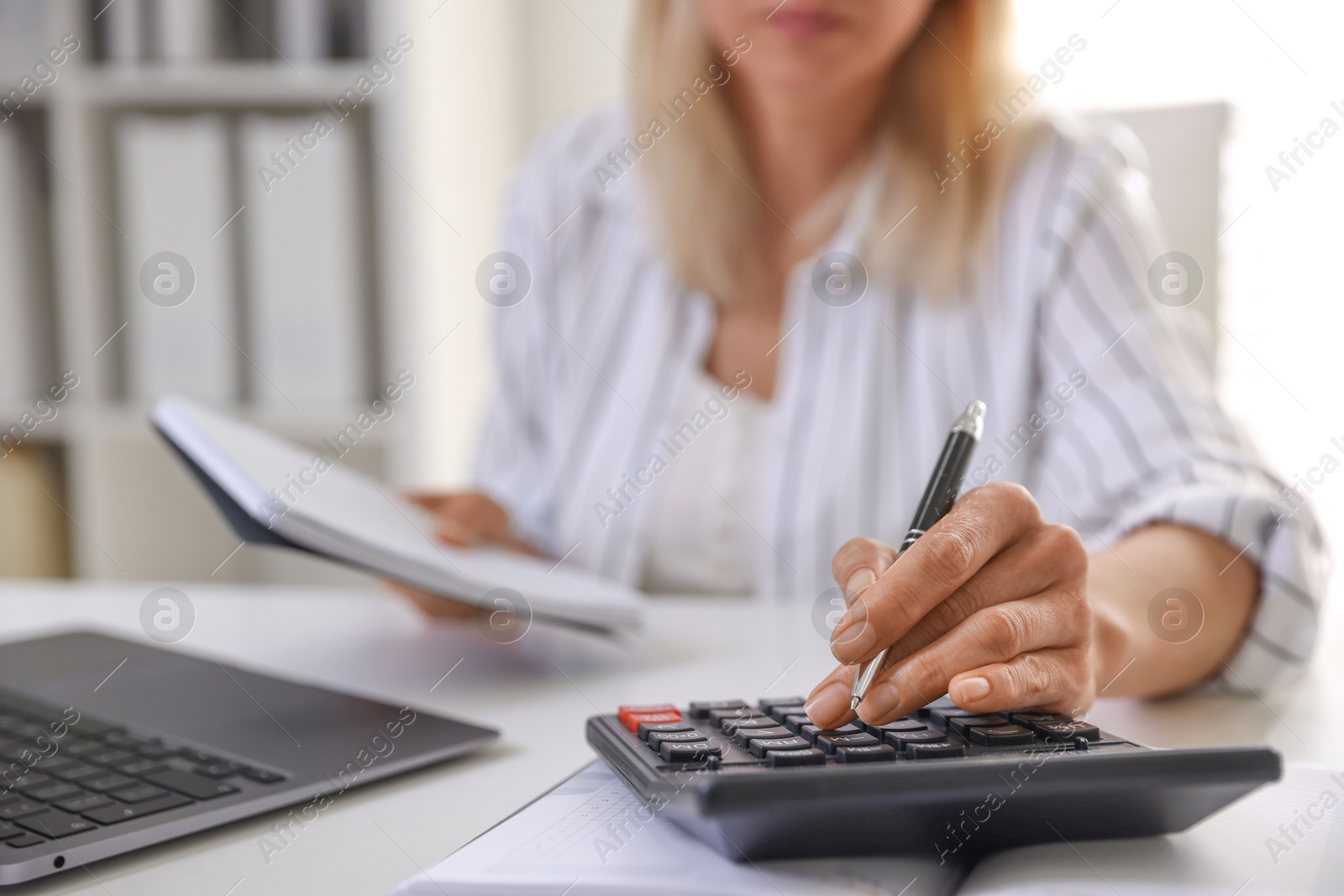 Photo of Budget planning. Woman with notebook using calculator at table indoors, closeup