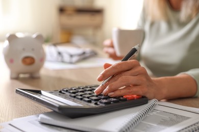 Photo of Budget planning. Woman with cup of drink using calculator at table indoors, closeup