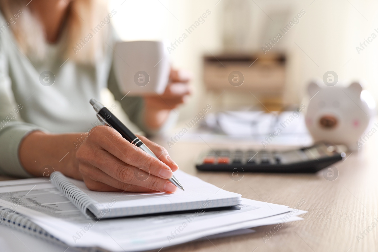 Photo of Budget planning. Woman with cup of drink taking notes at table indoors, closeup