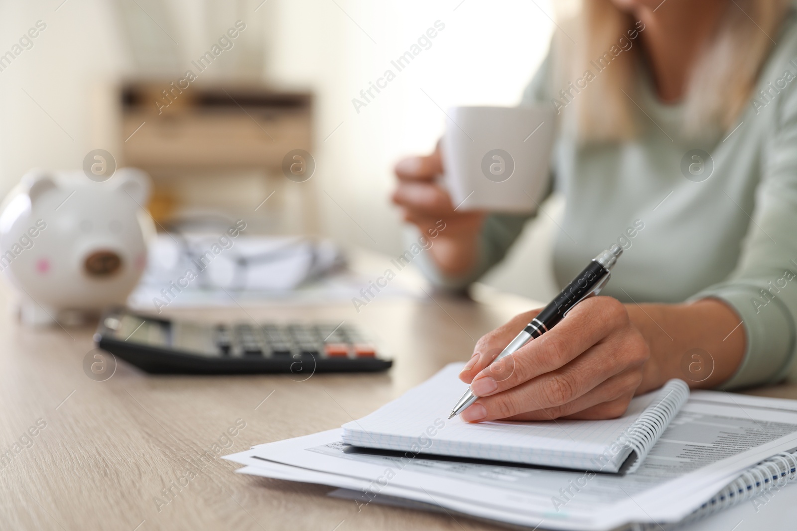 Photo of Budget planning. Woman with cup of drink taking notes at table indoors, closeup