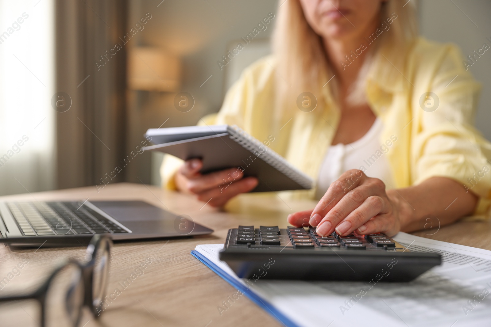 Photo of Budget planning. Woman with notebook using calculator at table indoors, closeup