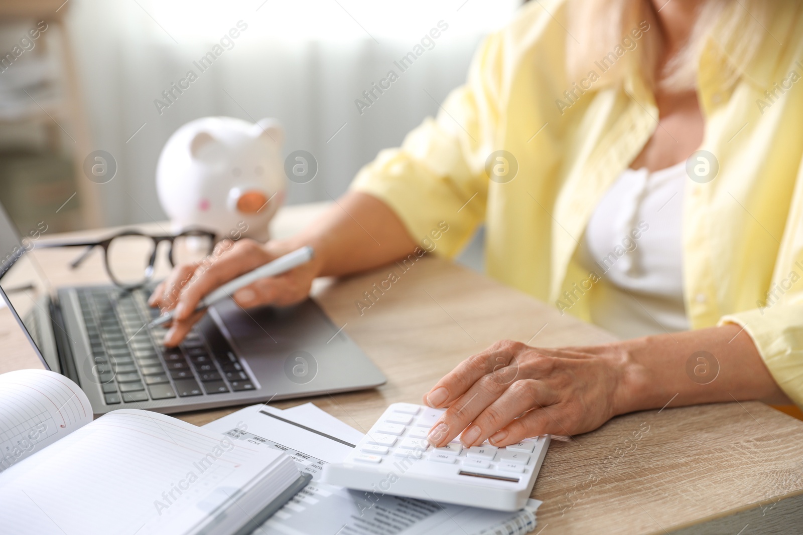 Photo of Budget planning. Woman working on laptop while using calculator at table indoors, closeup