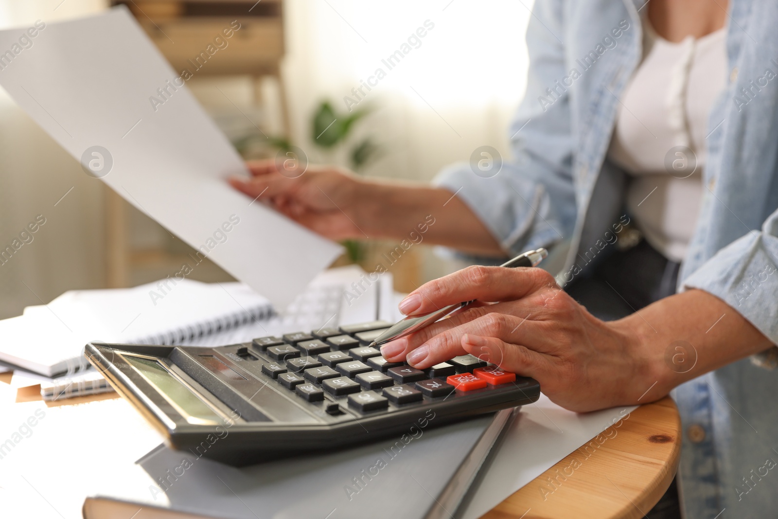 Photo of Budget planning. Woman using calculator while working with accounting document at table indoors, closeup