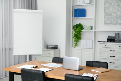 Photo of Flip chart, wooden table and chairs in conference room. Mockup for design