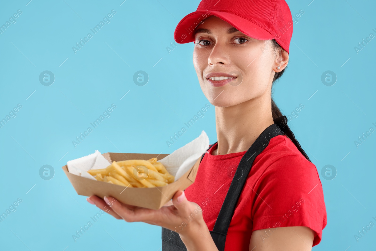 Photo of Fast-food worker holding paper container with fries on light blue background