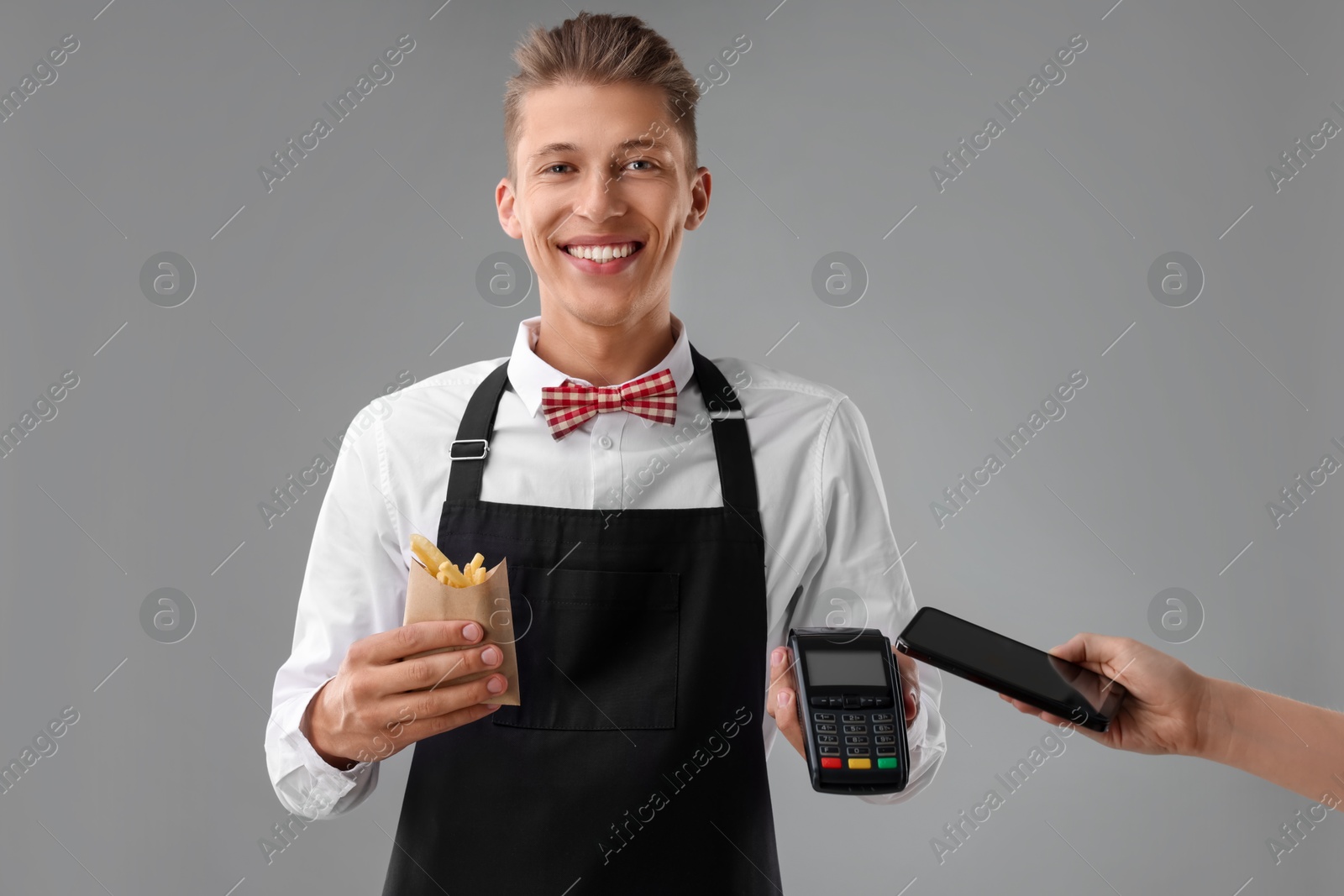 Photo of Fast-food worker taking payment from client via terminal on gray background, closeup