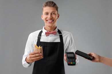 Fast-food worker taking payment from client via terminal on gray background, closeup