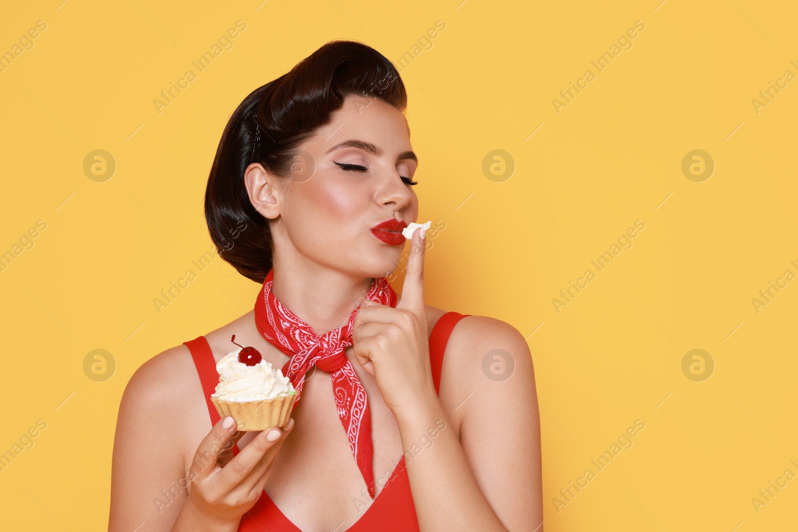 Photo of Pin-up woman eating cupcake on orange background, space for text